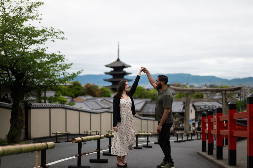 Couple dancing hand in hand on a street with red wooden railings and a traditional Japanese pagoda in the background.