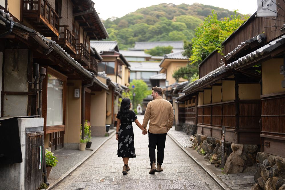 Couple holding hands strolling down a quiet stone-paved lane lined with traditional wooden houses in a historic Japanese district.