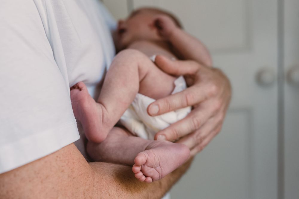 Close-up of a parent's hands gently cradling a newborn baby's tiny feet and legs.