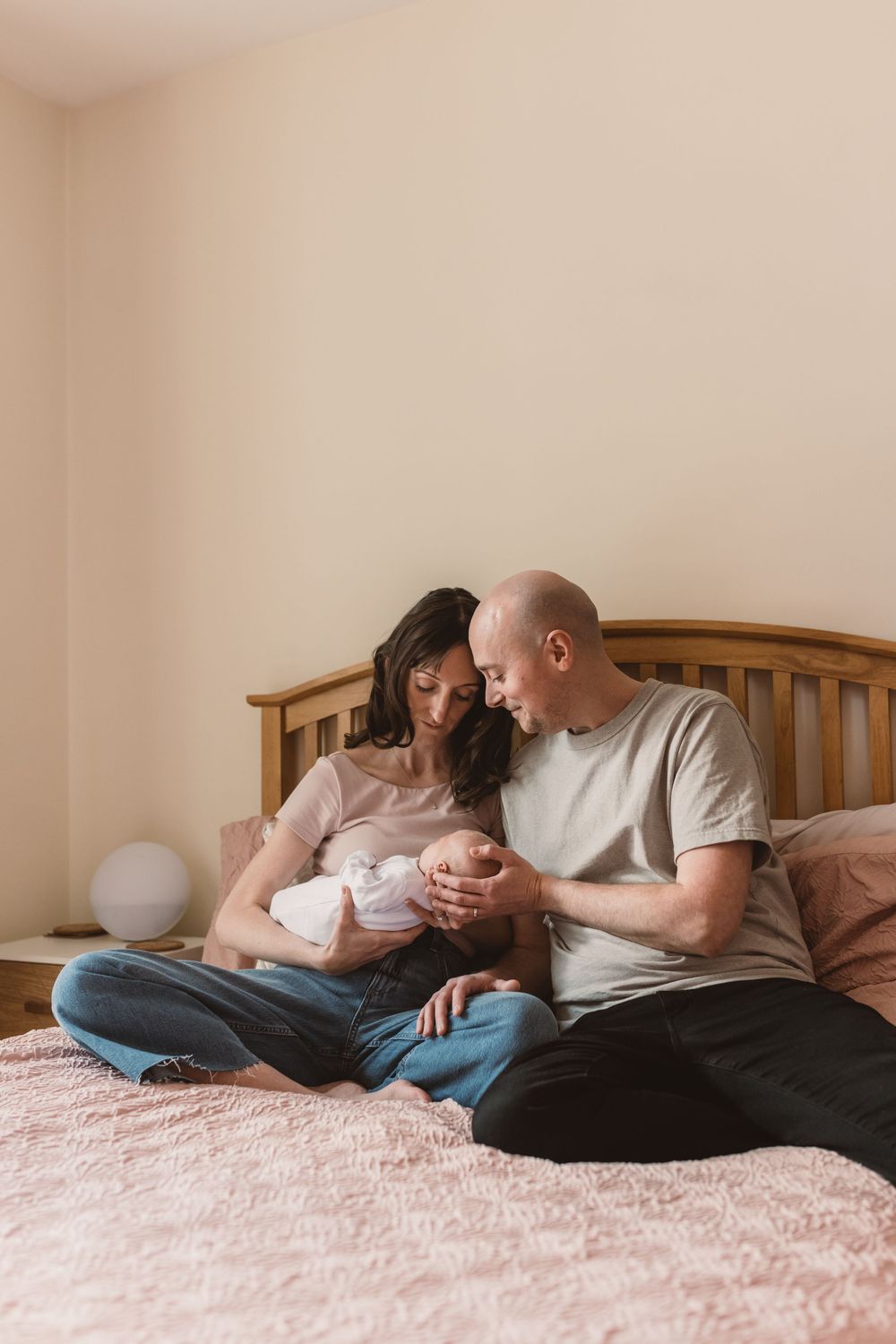 A couple sits on a bed gazing lovingly at their newborn baby, capturing a tender family moment at home.