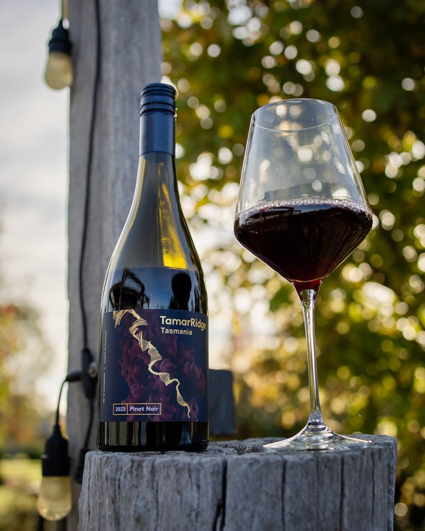 TamarRidge Tasmania Pinot Noir wine bottle and filled glass on rustic wooden post with bokeh garden background.