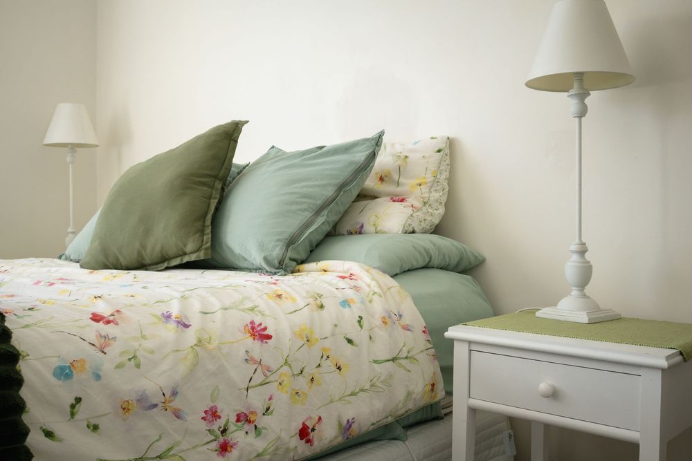 Bright bedroom with floral bedding, green pillows, and a white bedside table with lamp.
