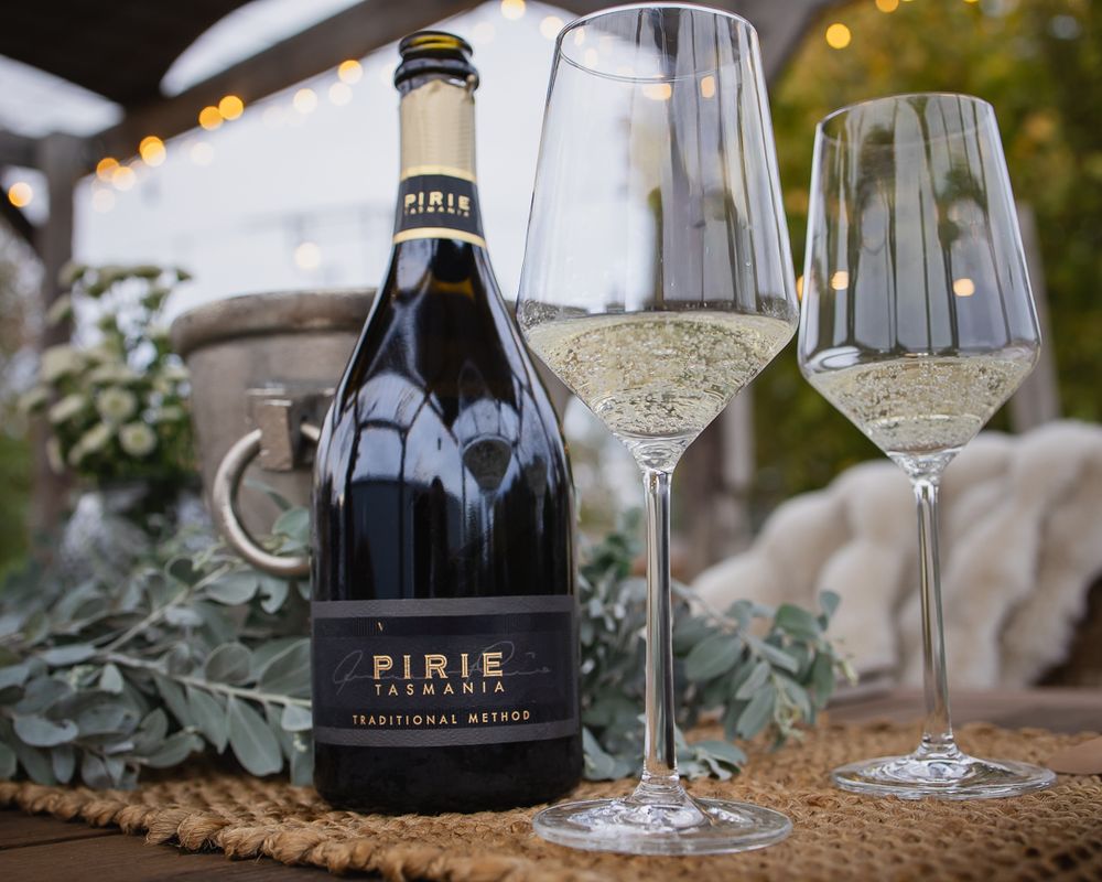 Pirie Tasmania Traditional Method sparkling wine bottle beside two elegant crystal glasses filled with bubbly white wine.