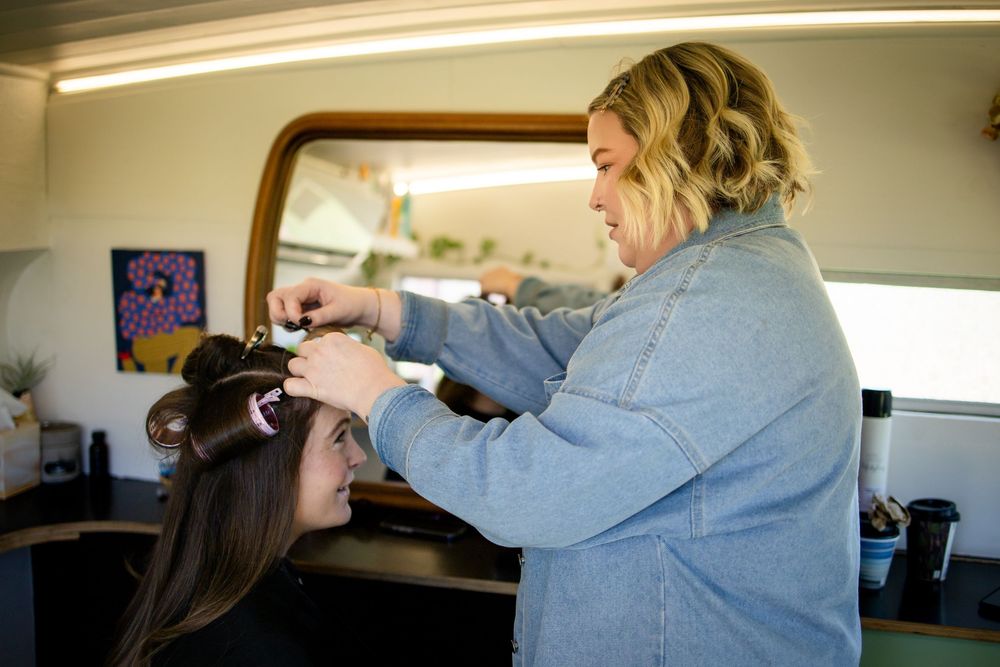 A hairstylist curling a brunette client's hair in a modern salon setting.