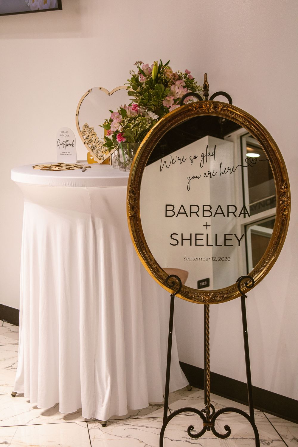 Gold oval mirror wedding welcome sign for Barbara and Shelley, September 2020, displayed on an easel beside a white draped table.
