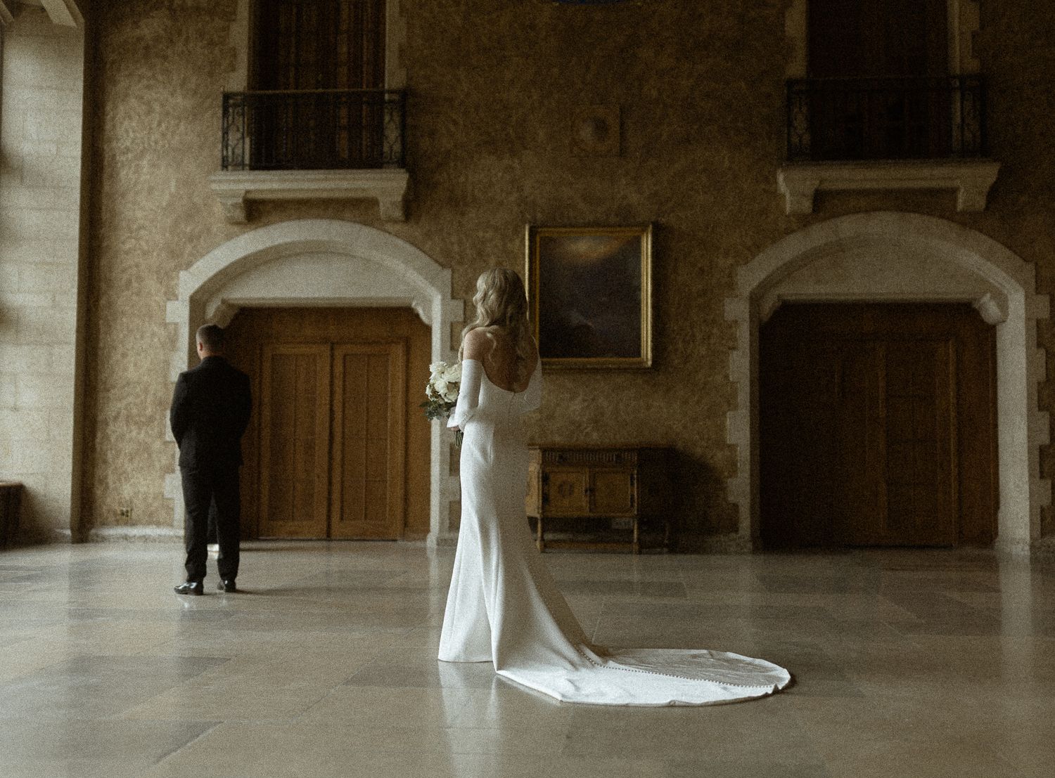 First look in a grand stone hall as the bride walks up behind her groom, by a Banff wedding photographer