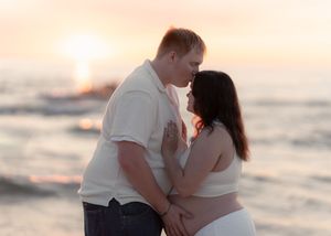 Couple sharing a romantic moment at sunset on the beach, golden light glowing behind them near the ocean.
