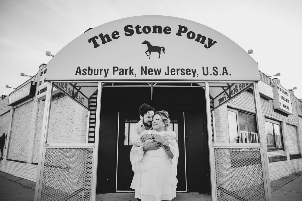 Couple embraces outside The Stone Pony music venue in Asbury Park, New Jersey in black and white wedding photo.