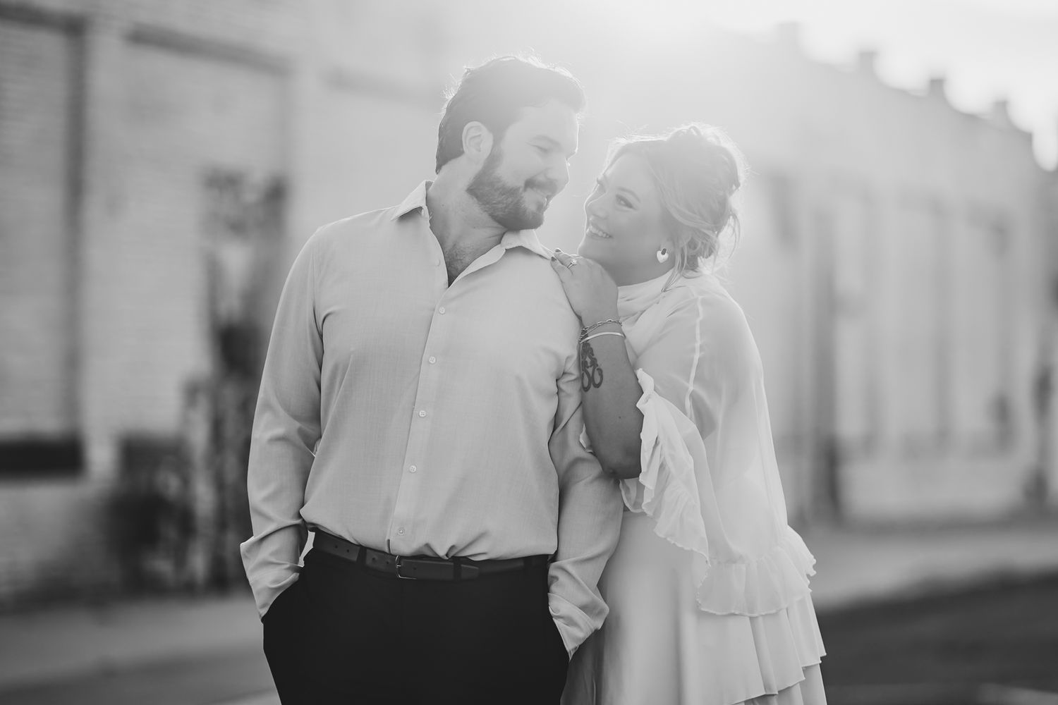 Black and white photo of a couple gazing at each other in soft backlight on a sunny street.