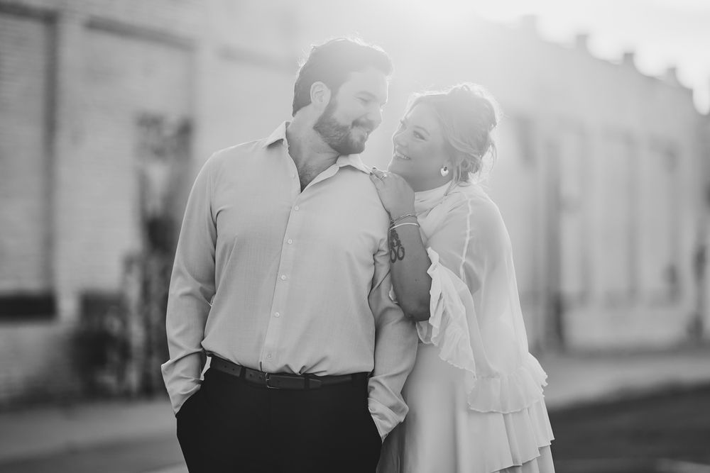 Black and white photo of a couple gazing at each other in soft backlight on a sunny street.