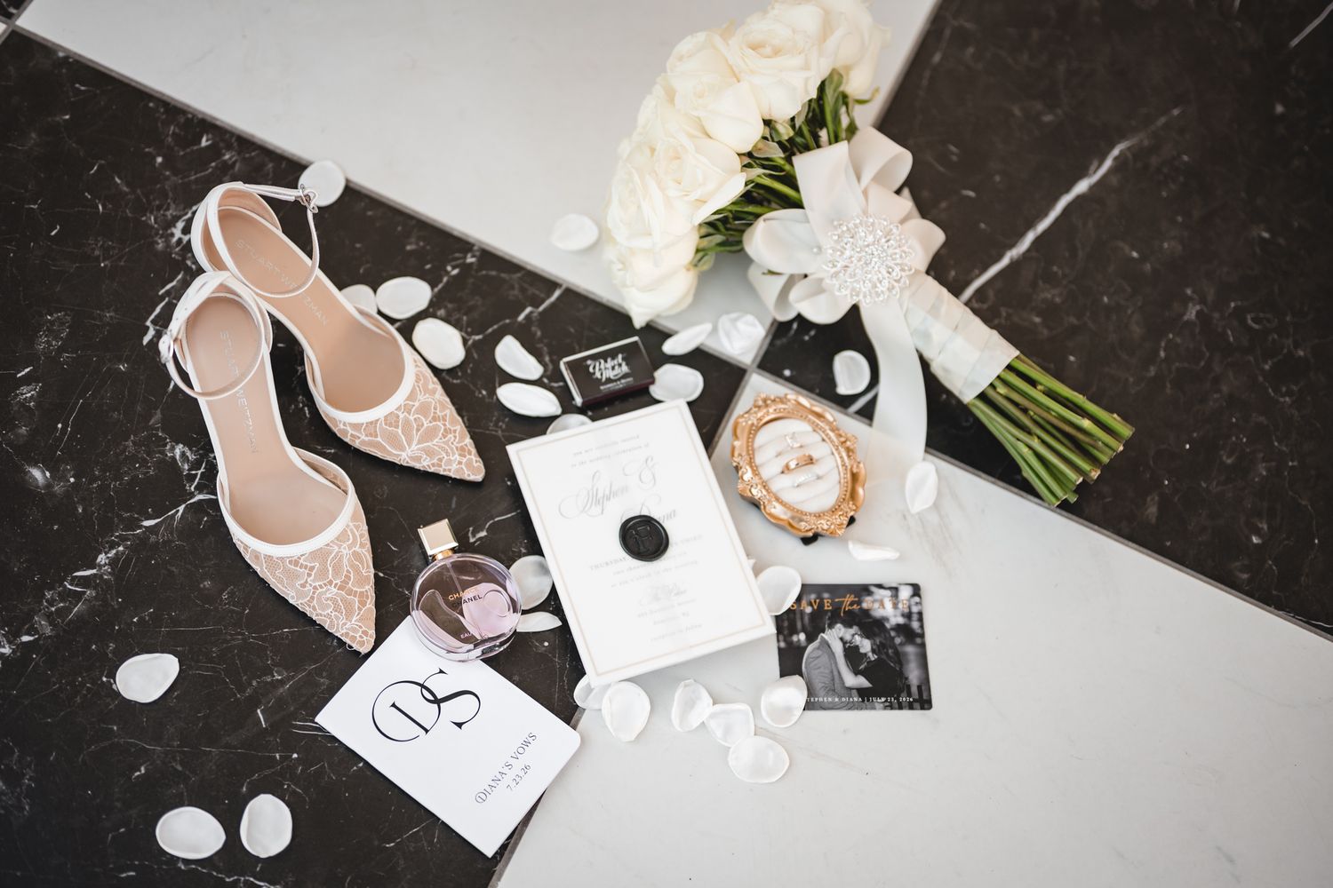 Elegant bridal flat lay with lace heels, white rose bouquet, perfume, gold watch, and wedding stationery on marble.
