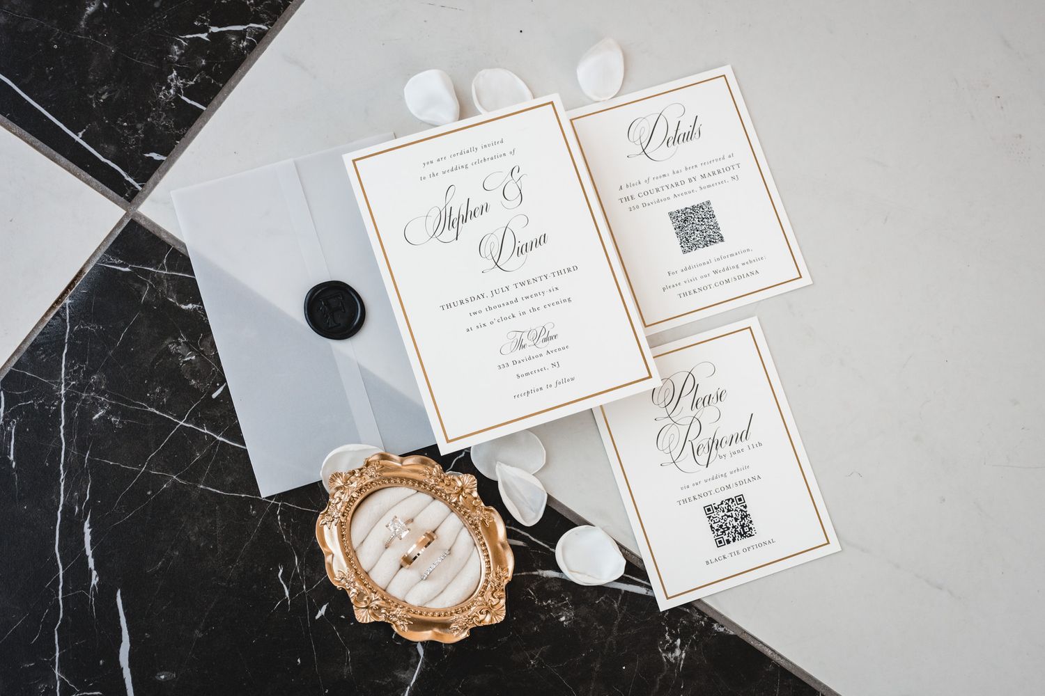Elegant wedding invitation suite with gold borders, QR codes, wax seal, and ring display on marble surface.