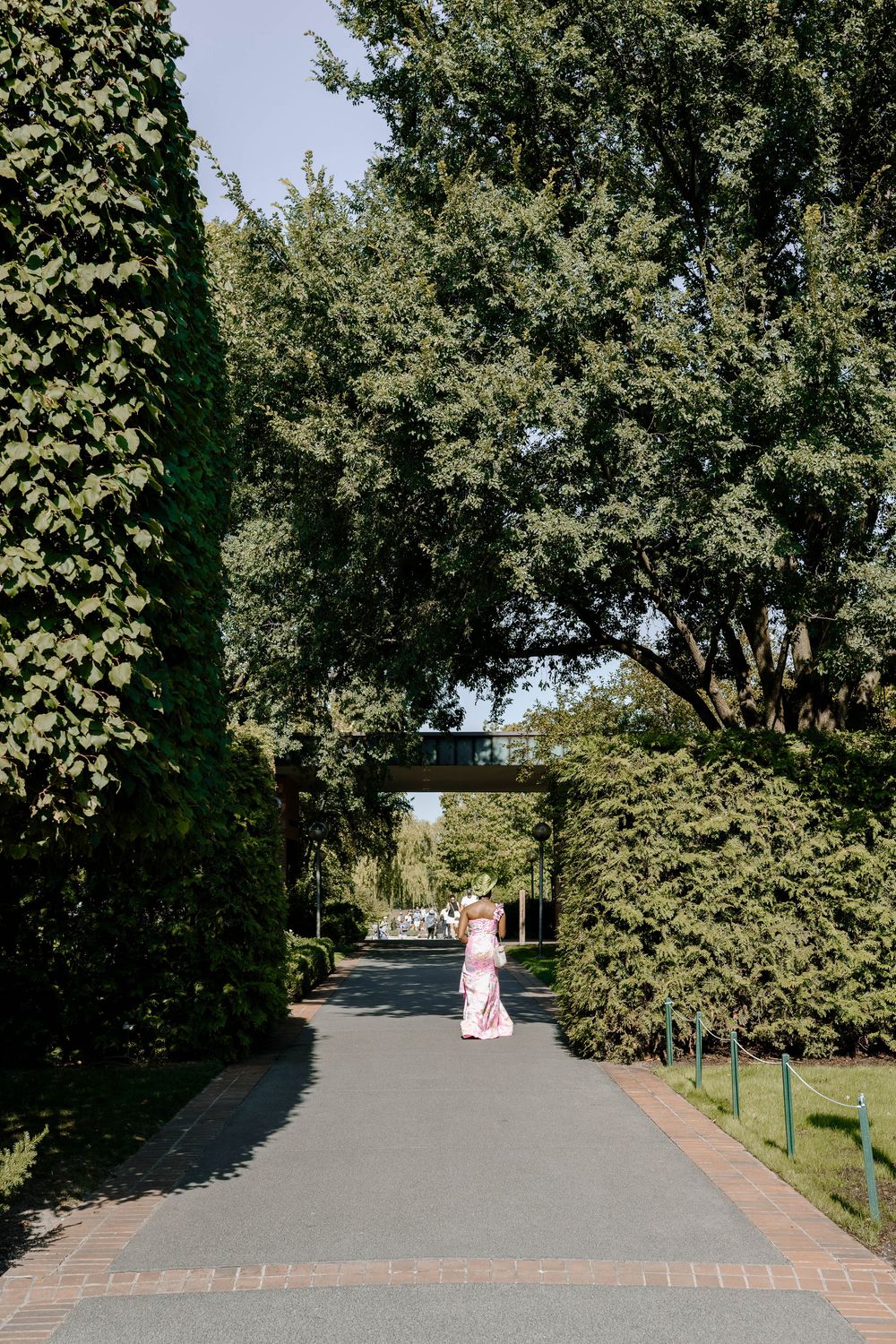 Bride in pink dress walking through lush garden archway on sunny wedding day.