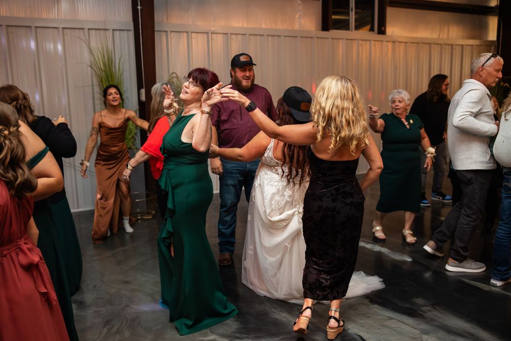Wedding guests in formal dresses and suits dance together with arms raised on a lively reception dance floor.