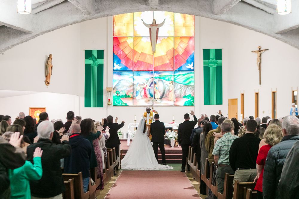 Bride and groom stand at the altar during a Catholic wedding ceremony as guests fill the church pews beneath a stained glass window.