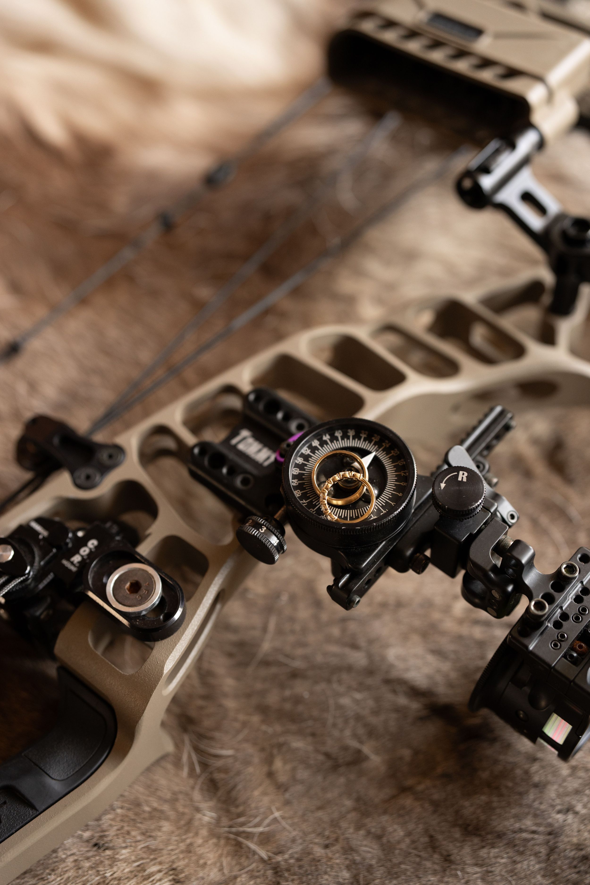 Close-up of a tan compound bow with a precision multi-pin sight and mounted accessories resting on a natural animal fur surface.