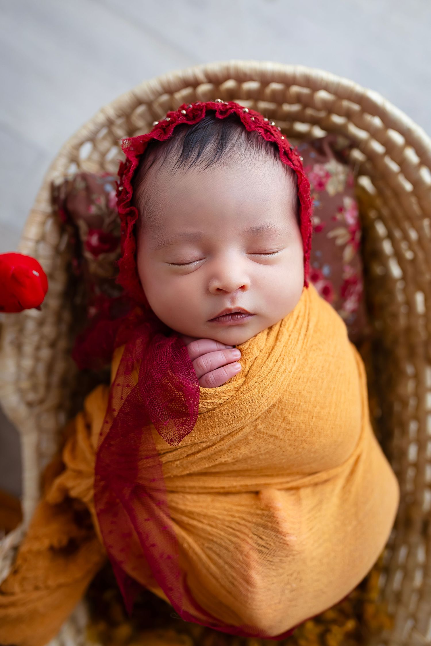 Bebe recien nacida envuelta en pano coloc naranja con gorrito color rojo vino dentro de una canasta