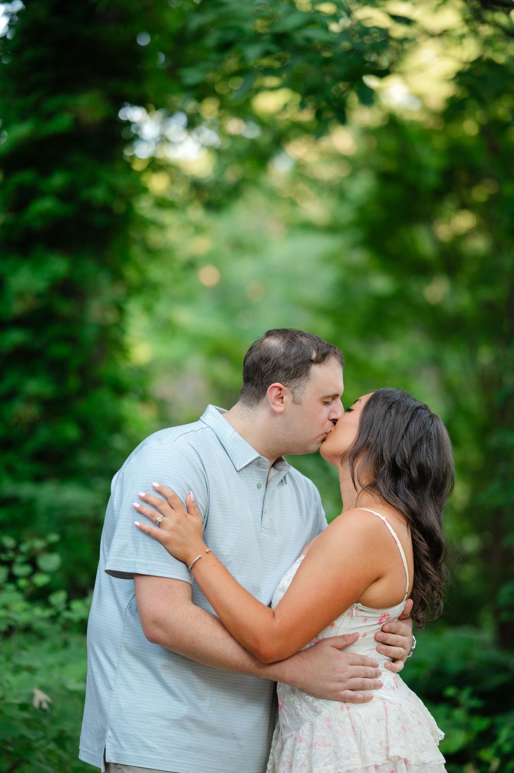 Engaged couple sharing a romantic kiss surrounded by vibrant green foliage during outdoor photo session.