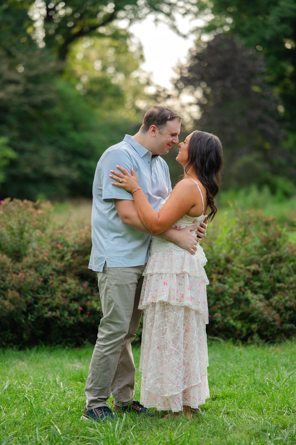 Couple sharing a romantic almost-kiss embrace in a lush green garden during golden hour engagement photos.