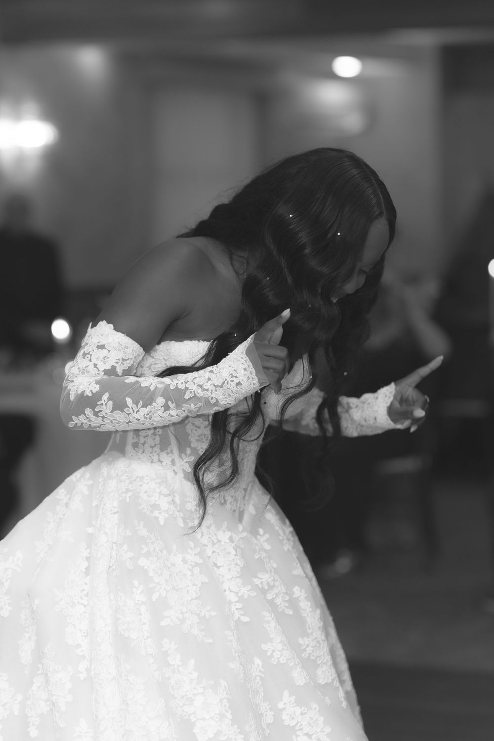 Black and white photo of a bride in lace off-shoulder gown dancing at her wedding reception.