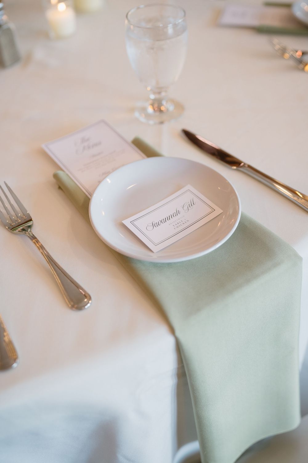 Elegant wedding place setting with mint green napkin, white plate, place card reading Savannah Gil, silverware, and glassware.
