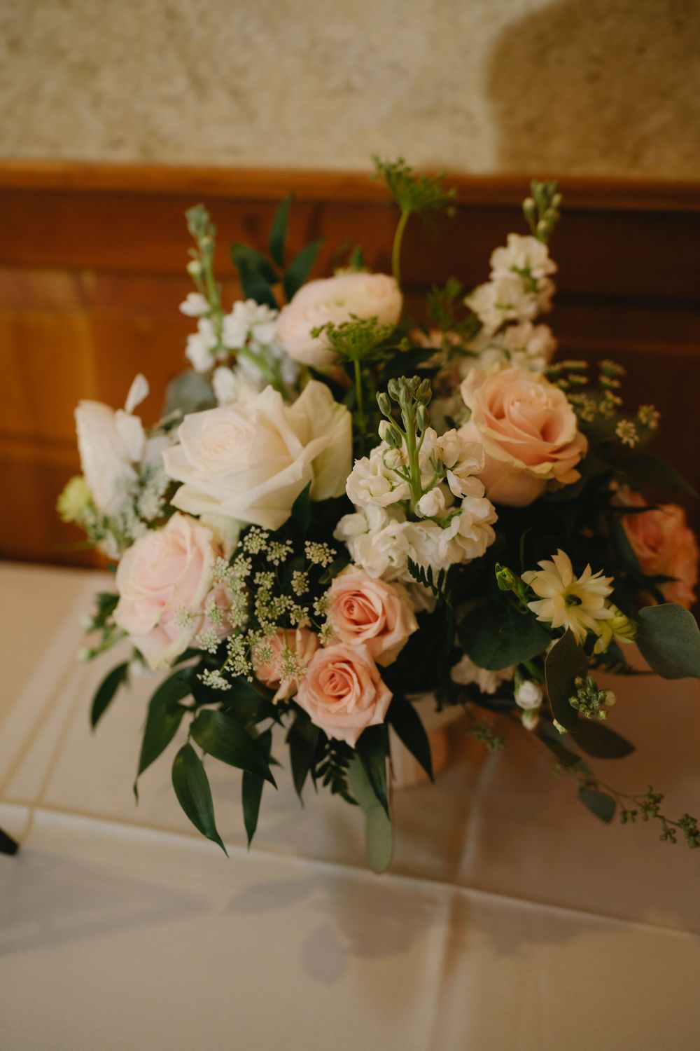 Romantic bridal floral arrangement featuring blush pink and white roses with lush greenery on a white surface.