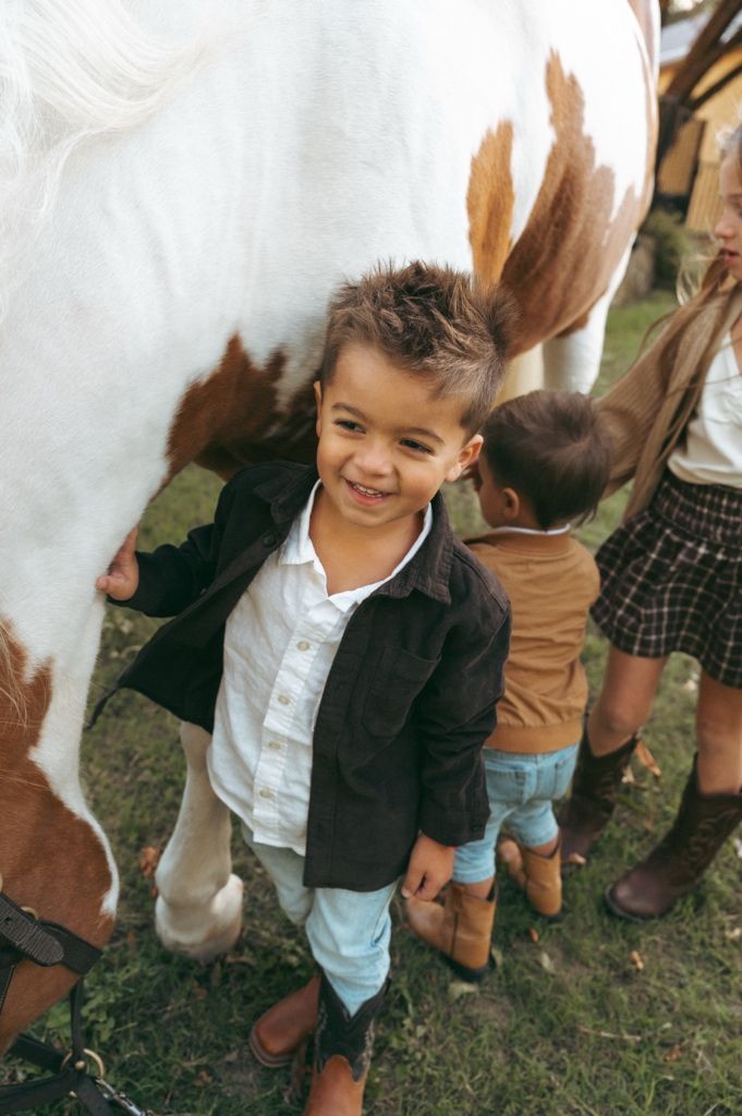Young boy giggling and reaching to pet a horse during a candid family photography session at Windmill Stables.