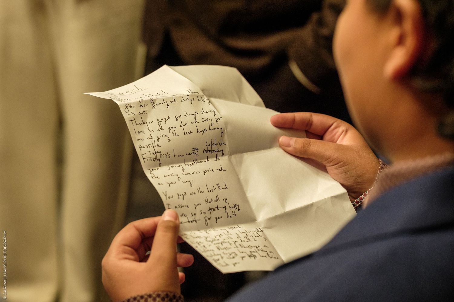 Person in a blue jacket reading a handwritten letter on folded white paper held in both hands.