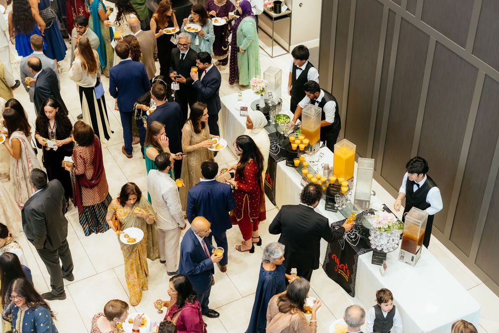 Overhead view of guests in formal and traditional attire mingling around a catering table with drinks and floral centerpieces at an elegant 