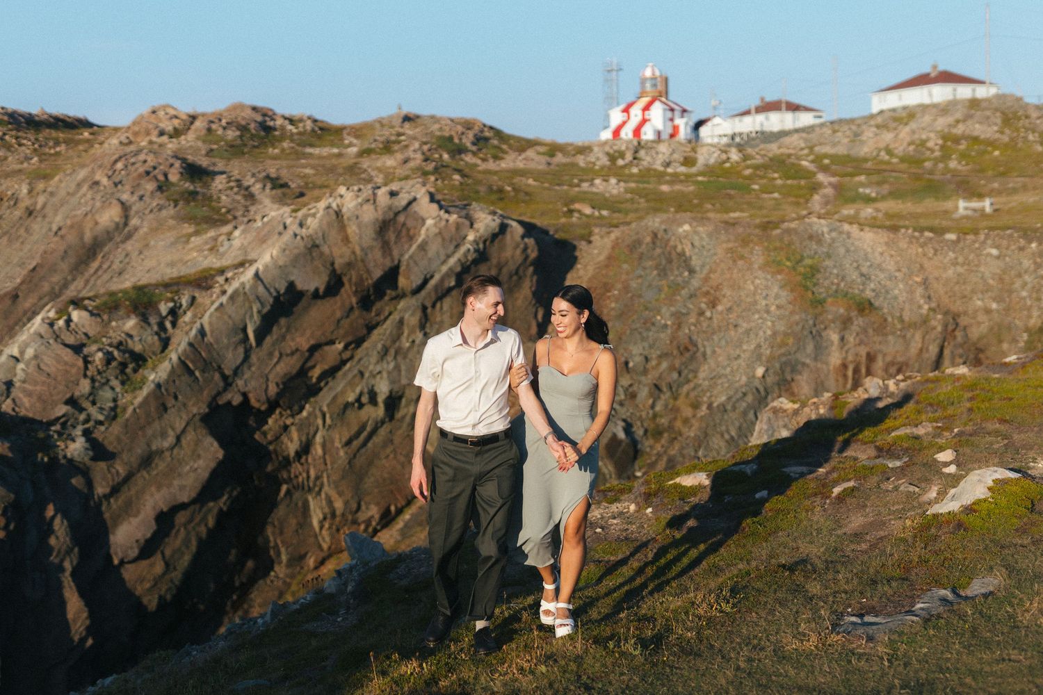 35 mm film photo of bride and groom walking along a rocky outcrop with a lighthouse behind them during elopement day