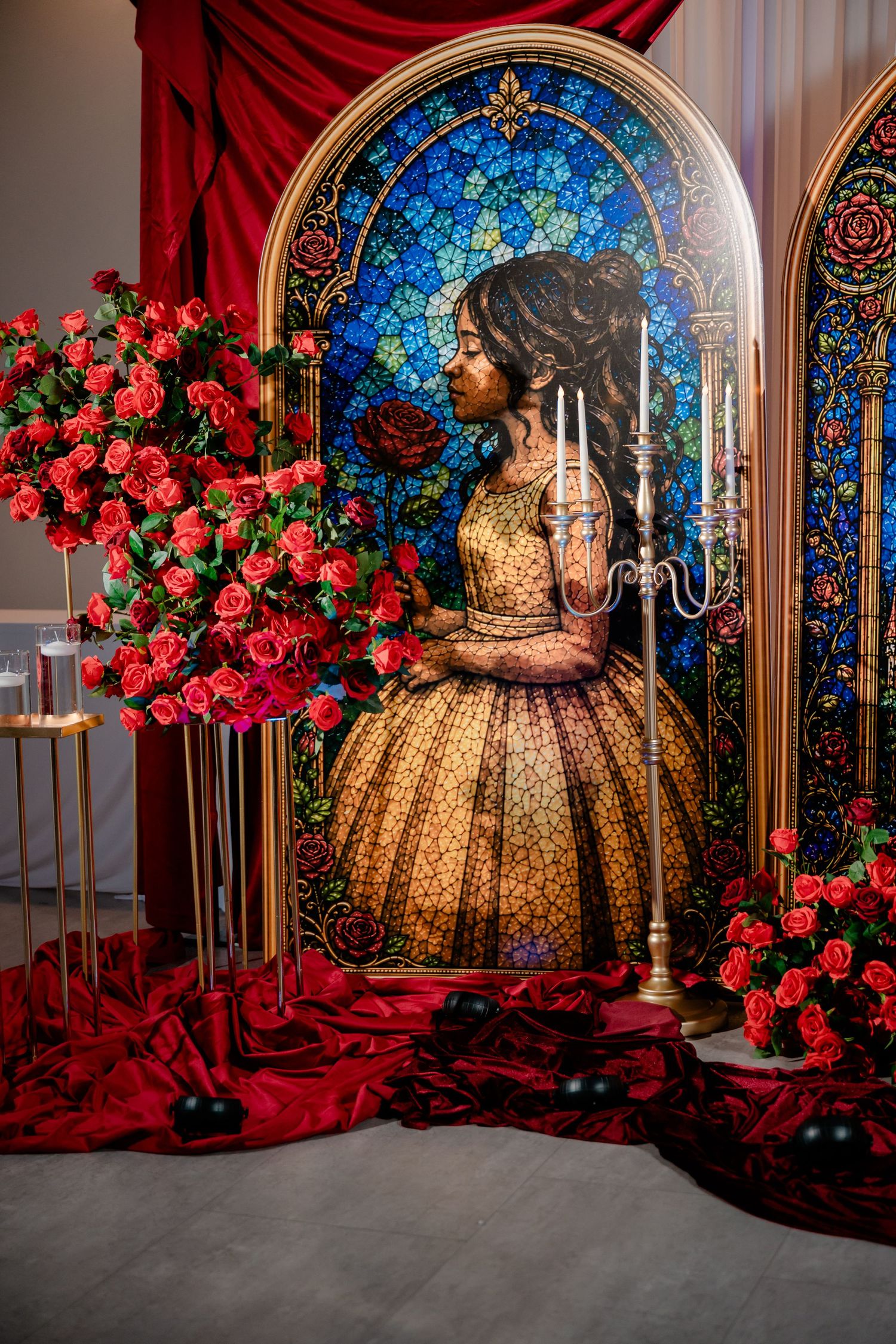 Stained glass-style Beauty and the Beast backdrop with a golden-gowned figure, red roses, candelabra and red draped fabric.