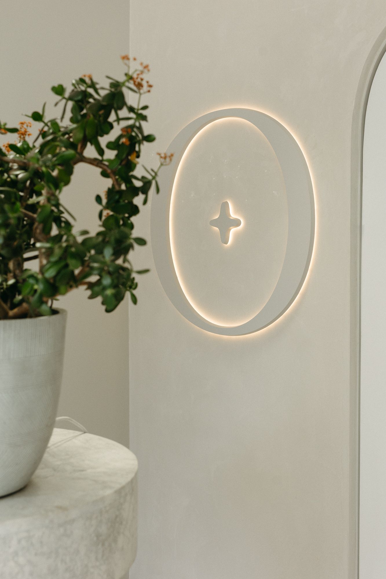 Circular LED wall light with star motif on white wall beside potted green plant on marble shelf.