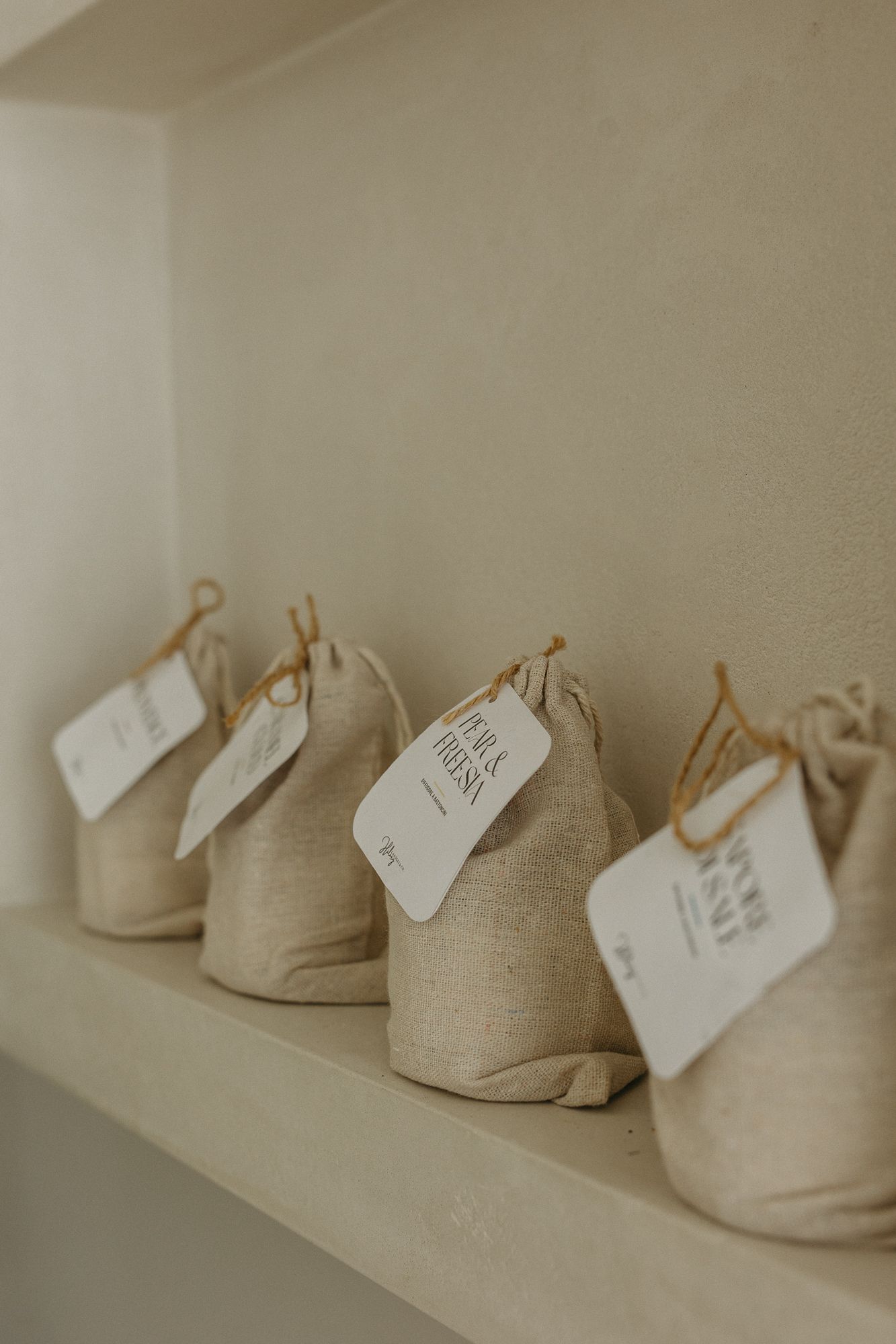 Small burlap drawstring bags with white tags displayed on a white shelf in a minimalist retail setting.