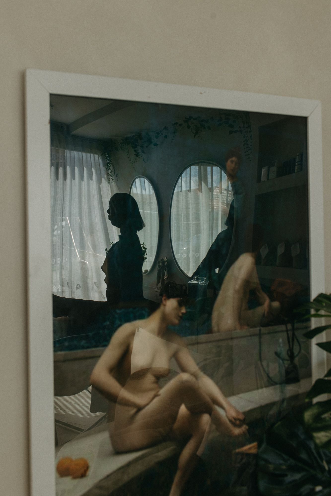A framed art photograph showing a figure in an interior room with oval mirrors and soft natural window light.