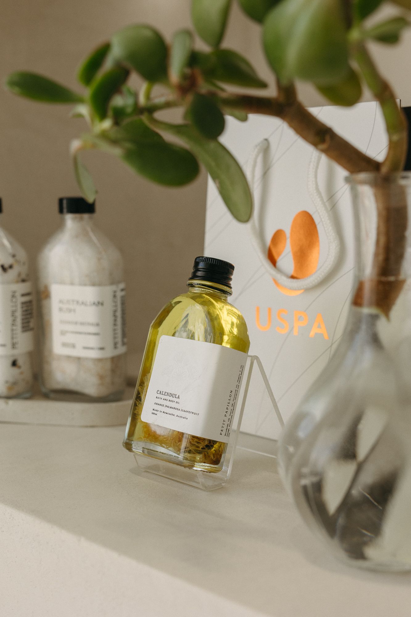 USPA branded gift bag with yellow body oil bottle and Australian Blur salt scrub on a white shelf.