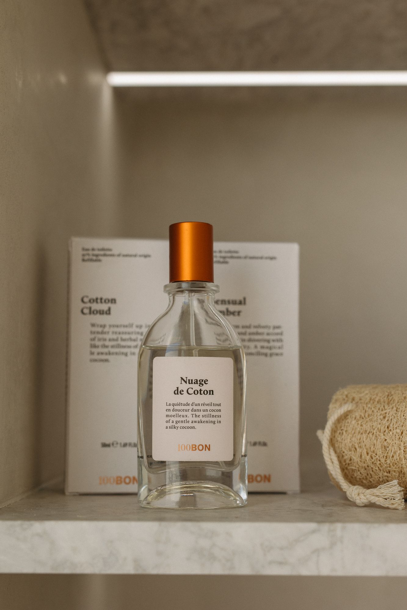 100BON Nuage de Coton perfume bottle with orange cap displayed on marble shelf beside loofah and product box.
