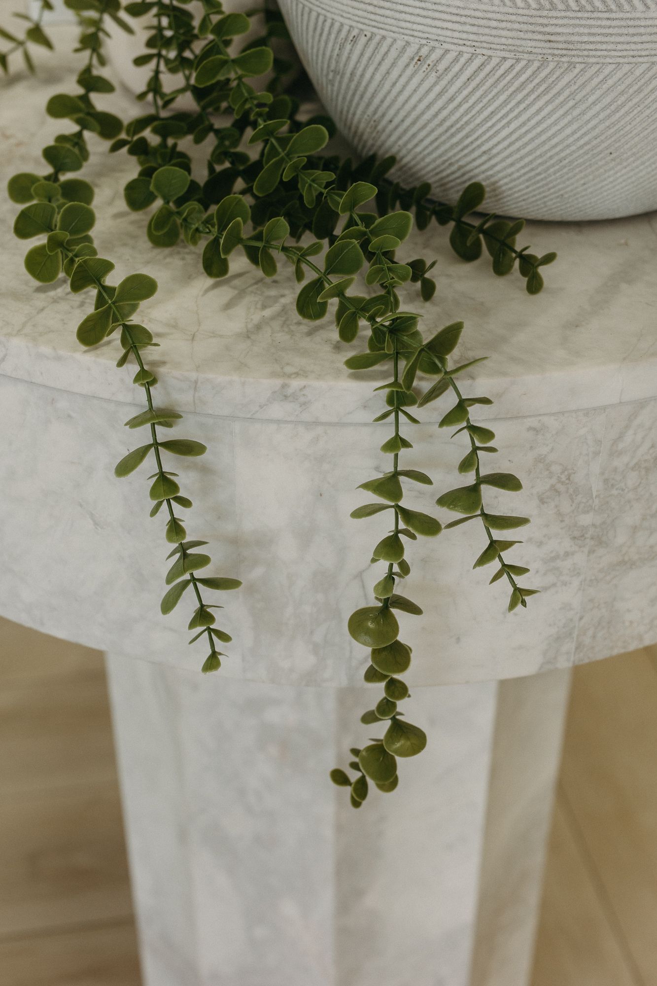Marble side table with trailing eucalyptus stems and a white textured ceramic vase on a light wood floor.