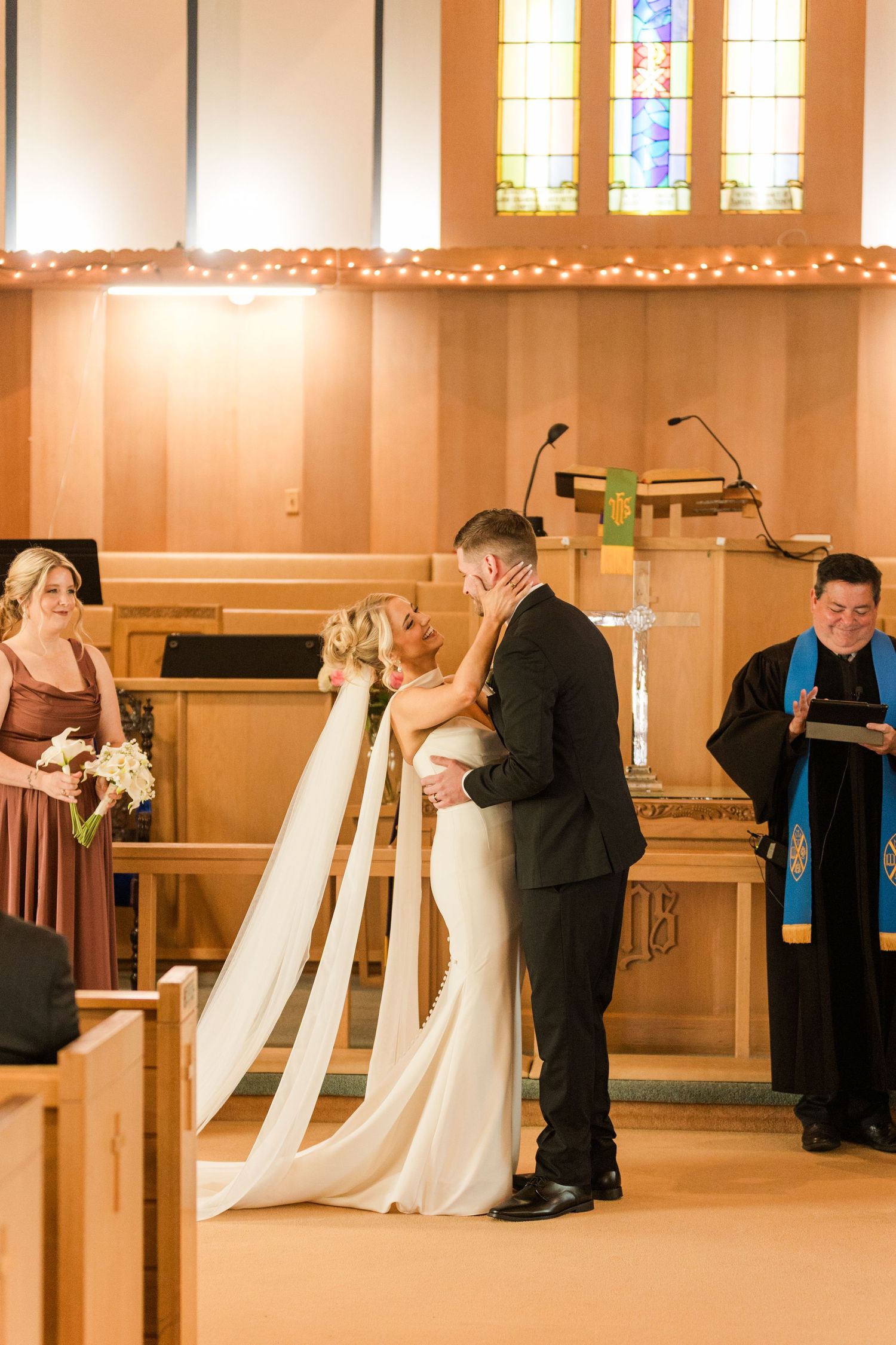 Bride and groom share their first kiss at the altar during a church wedding ceremony with stained glass windows.