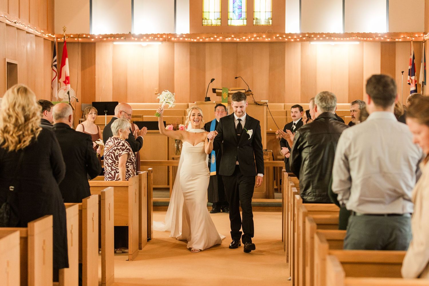 Bride and groom walk down the aisle of a warmly lit wooden church after their wedding ceremony.