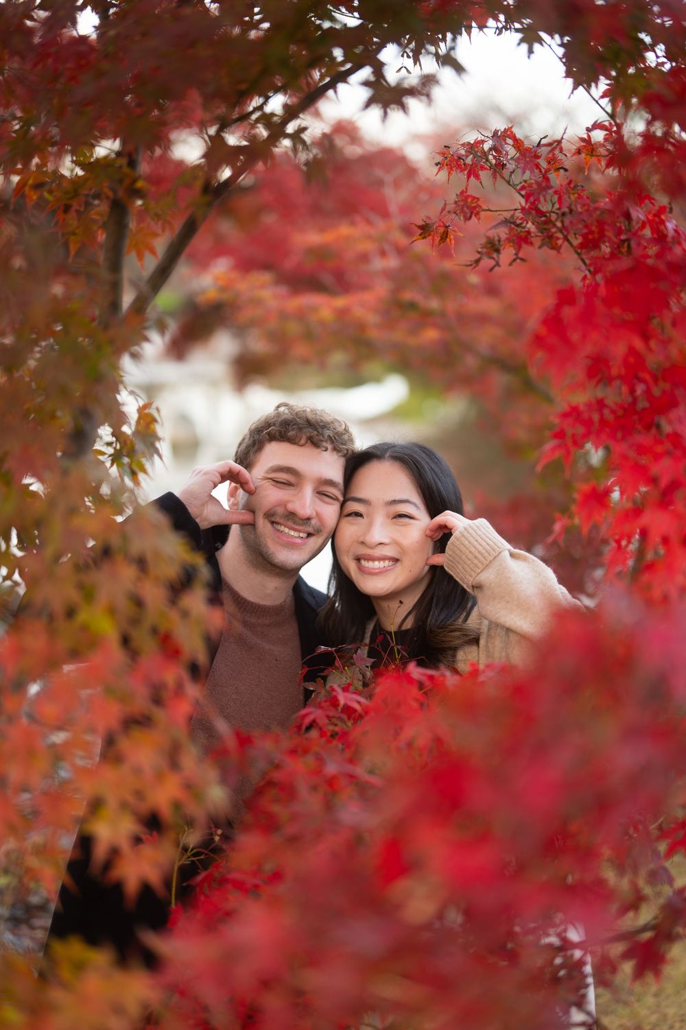 Couple smiling among vibrant red autumn maple leaves in a romantic fall foliage portrait.