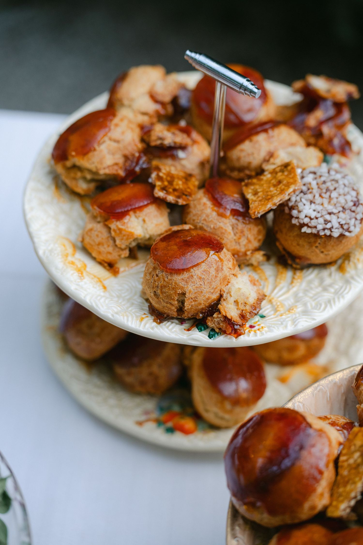 Two-tiered vintage plate stand filled with assorted pastries, scones, and glazed buns for afternoon tea service.
