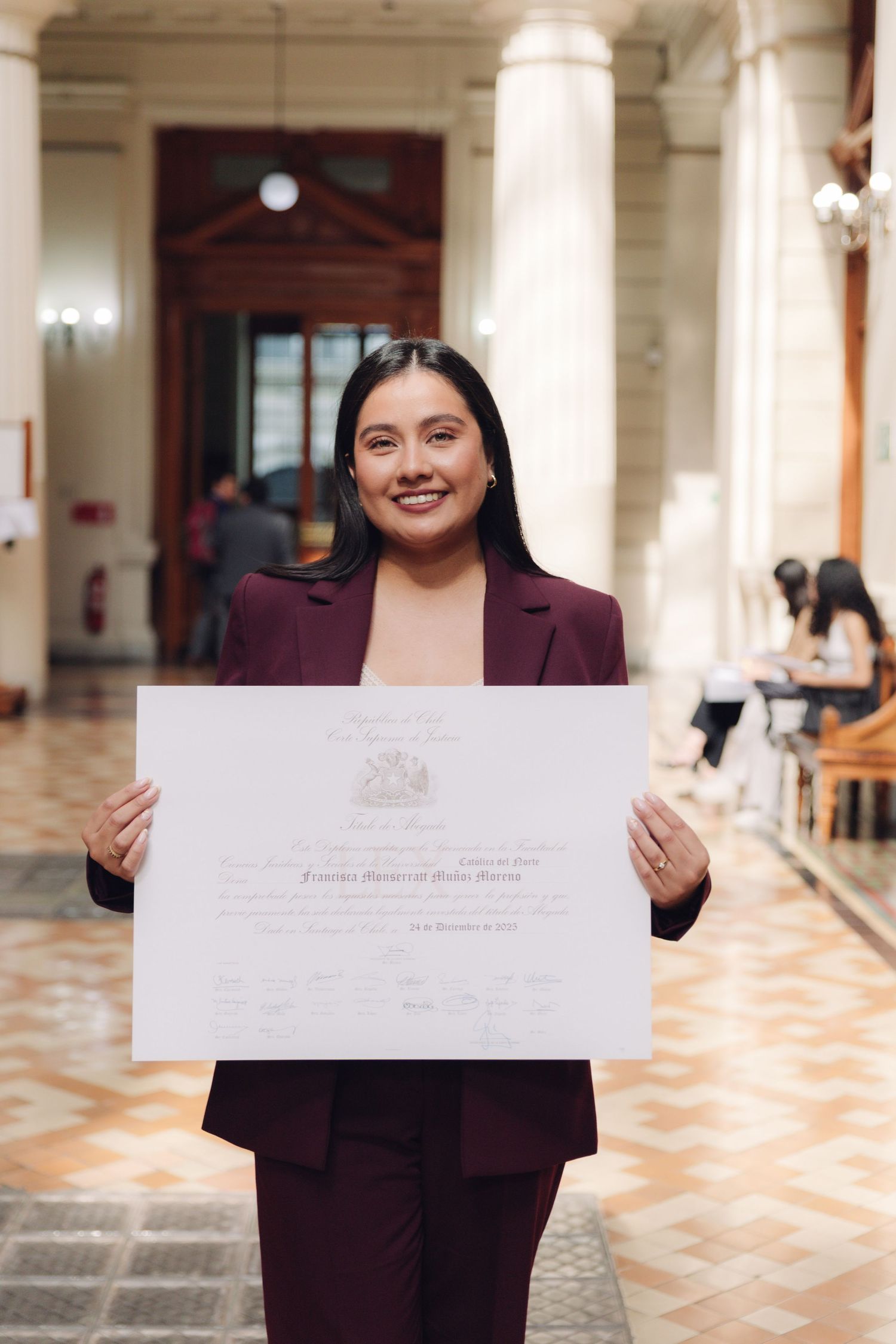 Happy woman in maroon suit displaying her diploma certificate in an elegant hall.