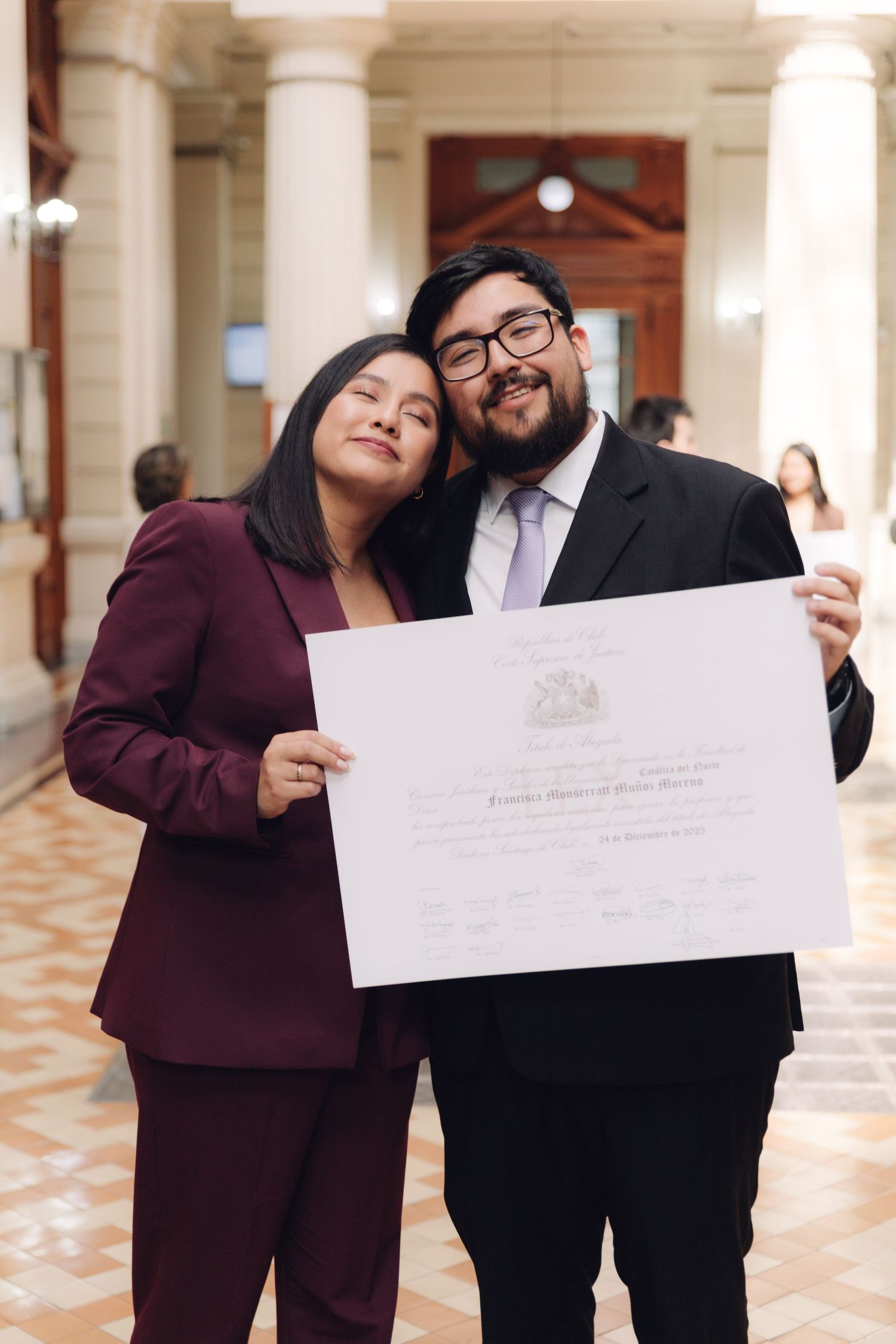 Woman in maroon suit and bearded man holding graduation diploma together.