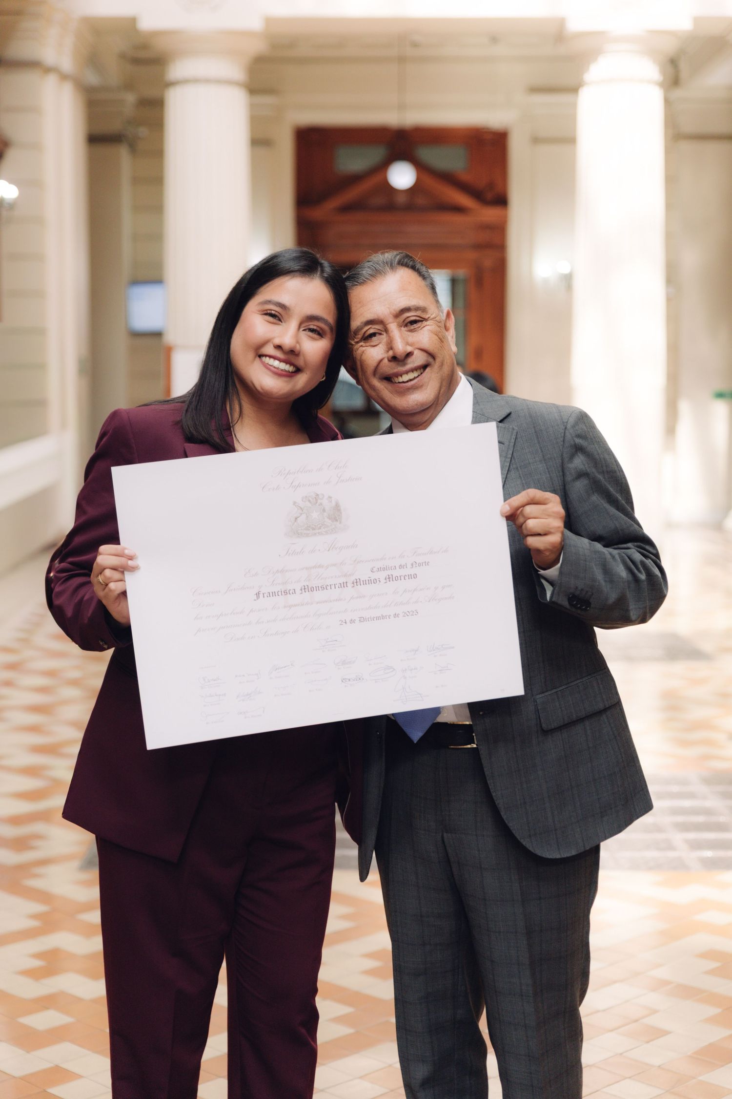 Smiling woman and older man proudly holding official certificate together in elegant corridor.