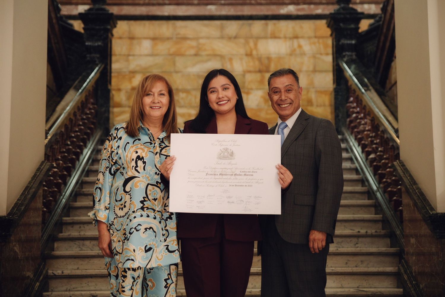 Female graduate celebrates with diploma alongside smiling parents on elegant staircase.