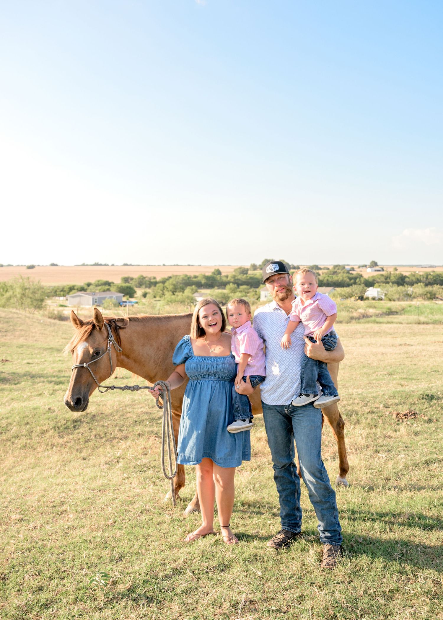 Family of four smiling outdoors with a chestnut horse on a sunny day in a green pasture in Taylor, TX
