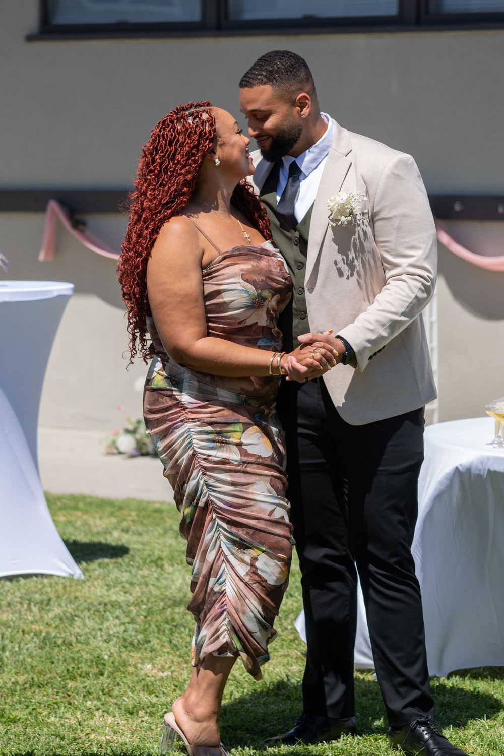 A couple shares a romantic dance outdoors at a wedding, man in tan blazer, woman in floral dress with red braids.