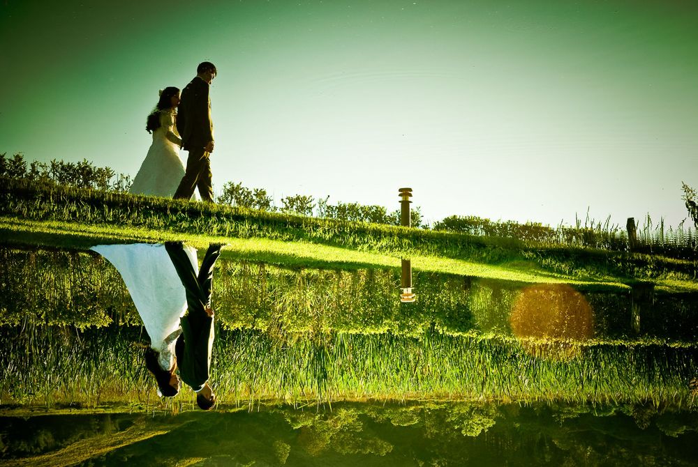 Couple walking on green grass reflected in water below, creating a stunning mirror image in a romantic outdoor setting.