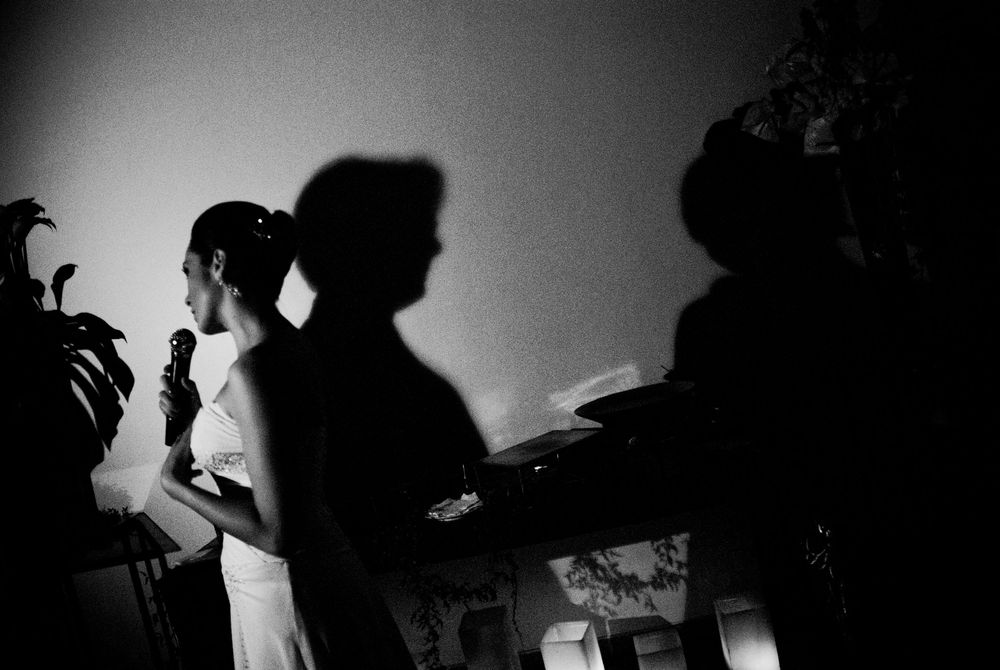 Black and white photo of a bride holding a microphone, with dramatic shadows cast on the wall behind her.