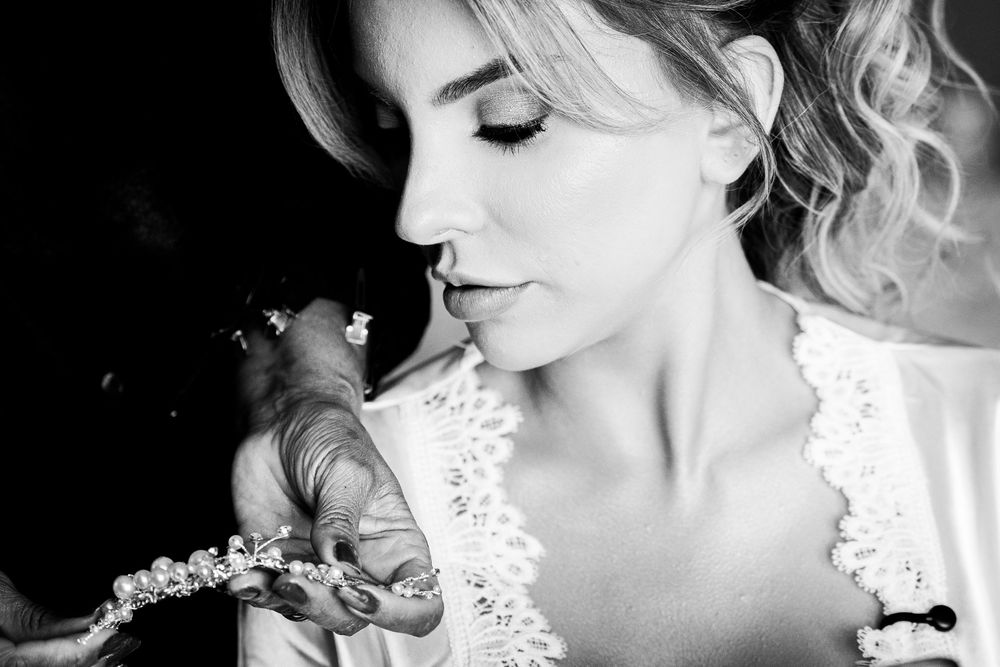 Black and white photo of a bride being helped with a floral hair accessory on her wedding day.